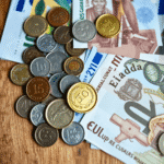 Prim-plan cu monede și bancnote internaționale diverse, aranjate artistic pe o suprafață de lemn, simbolizând moneda și schimbul valutar.