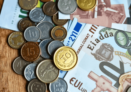 Prim-plan cu monede și bancnote internaționale diverse, aranjate artistic pe o suprafață de lemn, simbolizând moneda și schimbul valutar.